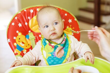 Mom feeds funny baby from a spoon . child eats in a highchairの写真素材
