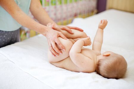 Mom Mom does gymnastics for a child. Mother massaging baby in a bed at homeの写真素材