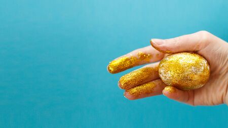 Easter golden egg in the hand on a blue background. Easter background. hand and egg in gold sparkles. bannerの写真素材