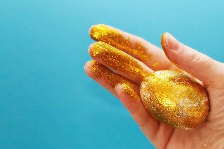 Easter golden egg in the hand on a blue background. Easter background. hand and egg in gold sparkles. happy Easterの写真素材