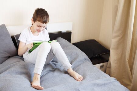 Distance learning online education. Boy sitting with a tablet on the bed in the room. Child with a gadget. Quarantine and self-isolation.の写真素材