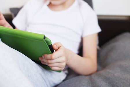 Distance learning online education. Boy sitting with a tablet on the bed in the room. Child with a gadget. Quarantine and self-isolation.の写真素材