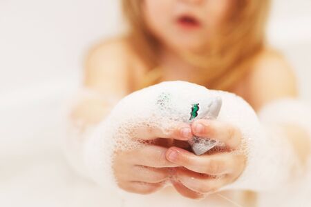 Funny little baby girl with blond hair playing with foam in a bath tub