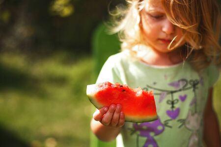 cute little girl holding a piece of watermelon in the gardenの写真素材
