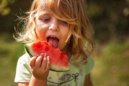 cute little girl holding a piece of watermelon in the gardenの写真素材