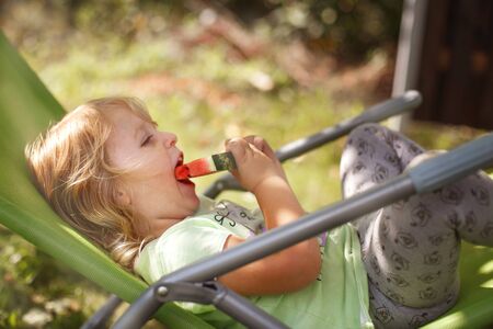 cute little girl eating watermelon on a deck chair in the gardenの写真素材