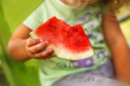 cute little girl holding a piece of watermelon in the gardenの写真素材