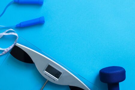Flat lay composition with weigh scales, skipping rope and dumbbells isolated on a blue background. Healthy active lifestyleの写真素材