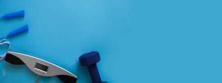 Woman measures her weight by standing her feet in socks on scale on a blue background with skipping rope and dumbbells. Flat lay composition. Healthy active lifestyleの写真素材