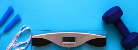 Woman measures her weight by standing her feet in socks on scale on a blue background with skipping rope and dumbbells. Flat lay composition. Healthy active lifestyleの写真素材