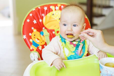 mother feeds funny baby from a spoon . child eats in a highchairの写真素材