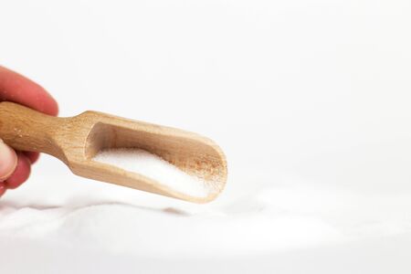 hand with a wooden spoon of salt grain on white backgroundの写真素材