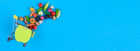 Metal shopping cart with fruits and vegetables on blue background. Toy miniature shopping trolleyの写真素材