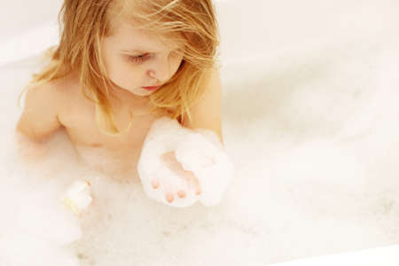 Funny little baby girl with blond hair playing with foam in a bath tub