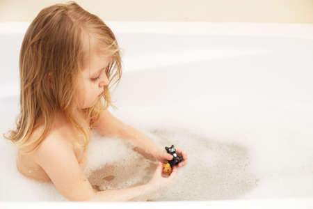 Funny little baby girl with blond hair playing with foam in a bath tubの写真素材
