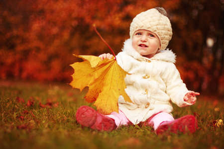 beautiful little baby girl sitting with a big leaf at autumn parkの素材 [FY310159535435]