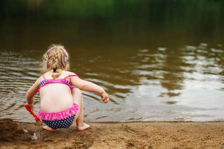 a small child plays in the sand. Beautiful girl sitting on the beach.の写真素材