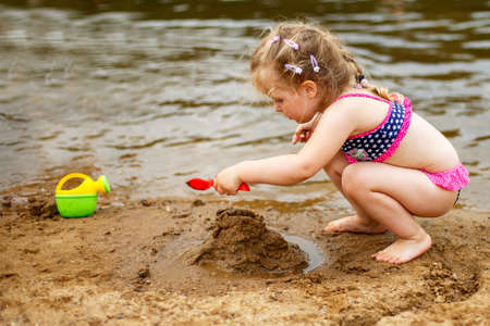 a small child plays in the sand. Beautiful girl sitting on the beach.の写真素材