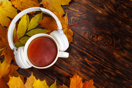 Cup of hot coffee or tea with autumn leaves and headphones on a brown wooden background