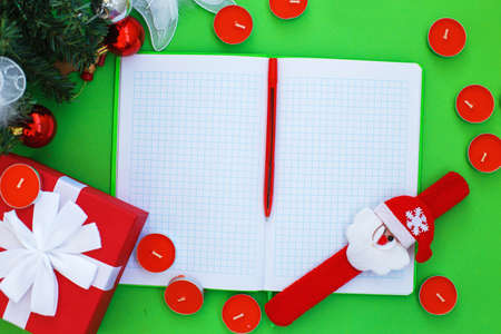 Christmas composition. Christmas gift, presrnt box, many red candles, notepad for writing and fir tree branches with toys on a green background. Top view. Flat lay.の写真素材