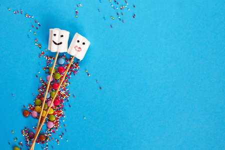 marshmallows composition on wooden skewers with color sweets on blue background. Flat lay, holiday...