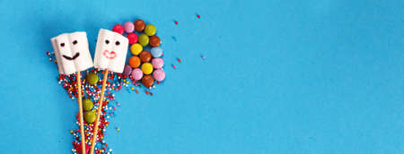 marshmallows composition on wooden skewers with color sweets on blue background. Flat lay, holiday concept. sweets in the form of people. bannerの写真素材