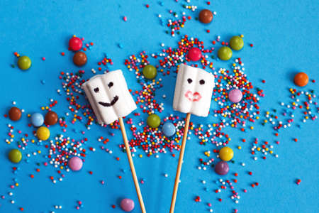 marshmallows composition on wooden skewers with color sweets on blue background. Flat lay, holiday concept. sweets in the form of peopleの写真素材