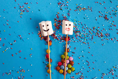 marshmallows composition on wooden skewers with color sweets on blue background. Flat lay, holiday concept. sweets in the form of peopleの写真素材