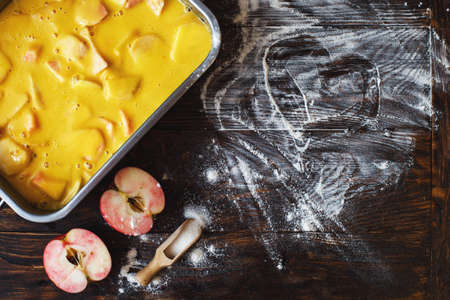Making an apple pie. Raw dough in a baking dish, apple, sugar and flour on the wooden backgroundの写真素材