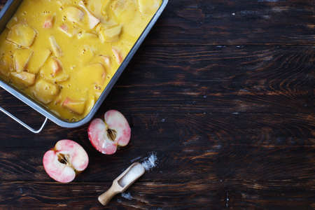 Making an apple pie. Raw dough in a baking dish, apple and sugar on the wooden backgroundの写真素材