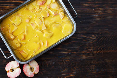 Making an apple pie. Raw dough in a baking dish, apple and sugar on the wooden backgroundの写真素材