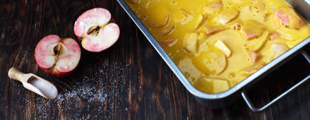 Making an apple pie. Raw dough in a baking dish, apple and sugar on the wooden background. bannerの写真素材