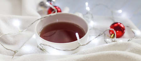 Cup of tea or coffee, knitted white blanket, garland and Christmas balls . christmas morning...