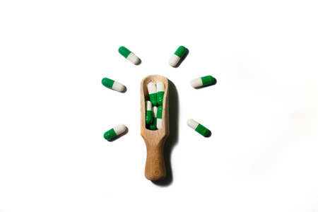 medicine green pills on white background on wooden spoon in the form of a light bulb.の写真素材