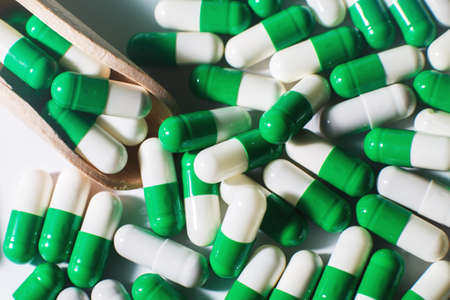 medicine green pills on white background on wooden spoon. sorted pharmaceuticalの写真素材