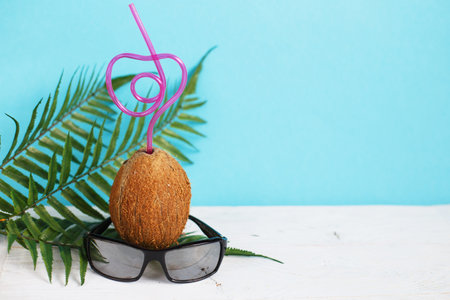 A coconut with straw and black sunglasses on a blue background. Summer and trave concept. copy spaceの写真素材