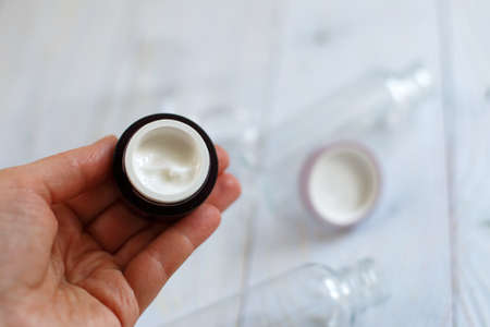 womans hands holding a jar of face cream on a natural light blue wooden backgroundの写真素材