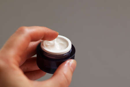 Hands of a girl with a jar of face cream close up applied to the finger of womans hand on light backgroundの写真素材