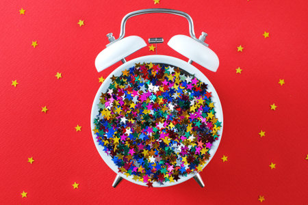 creative alarm clock and star shaped confetti on the red background. New year or Christmas concept....