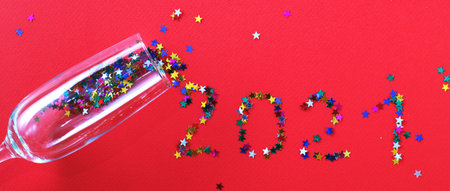 Champagne glass with star shaped sequins scattered in the form of inscription 2021 on a red background. Party, christmas, new year, celebration concept. banner. Top view. Flat lay.の写真素材