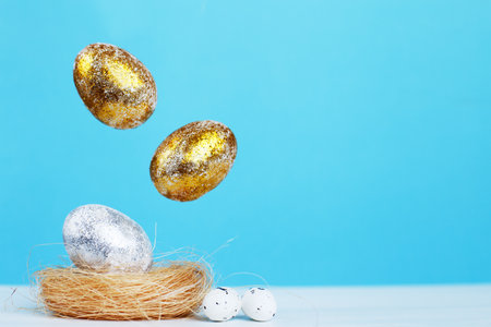 Gold and silver Easter eggs levitation to the nest on blue background. Easter concept. Copy spaceの写真素材