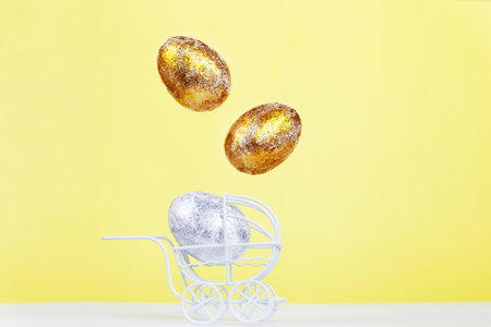 Easter golden and silver eggs levitation in the white baby stroller on a yellow background. Easter holiday concept. Newborn concept.の写真素材