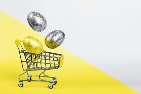 Easter golden and silver eggs levitation to the shopping cart on a Illuminating yellow and Ultimate Gray background. Easter concept. Copy space. Trendy colors of the 2021 yearの写真素材