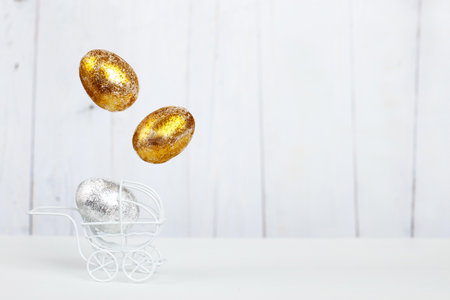 Easter golden and silver eggs levitation in the white baby stroller on a light wooden background. Easter holiday concept. Newborn concept.の写真素材