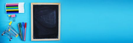 School chalkboard and stationery accessories, pencils and pens with a shopping cart. Back to school concept, top view, blue backgroundの写真素材