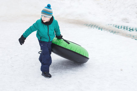 Child having fun on snow tube. Boy is riding a tubing. Winter entertainment. kid sliding downhill on a tube. boy dragging tubingの写真素材