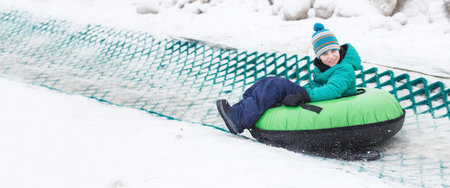 Child having fun on snow tube. Boy is riding a tubing. Winter entertainment. kid sliding downhill on a tube. bannerの写真素材