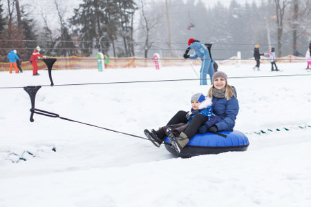 Family having fun on snow tube. mother with a kid is riding a tubing. Winter entertainment. people sliding downhill on tube. ride a liftの写真素材