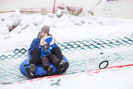 Family having fun on snow tube. mother with a kid is riding a tubing. Winter entertainment. people sliding downhill on tubeの写真素材