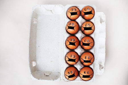 chicken eggs with drawn medical mask on egg carton on a white background. Easter eggs holidays decoration.の写真素材